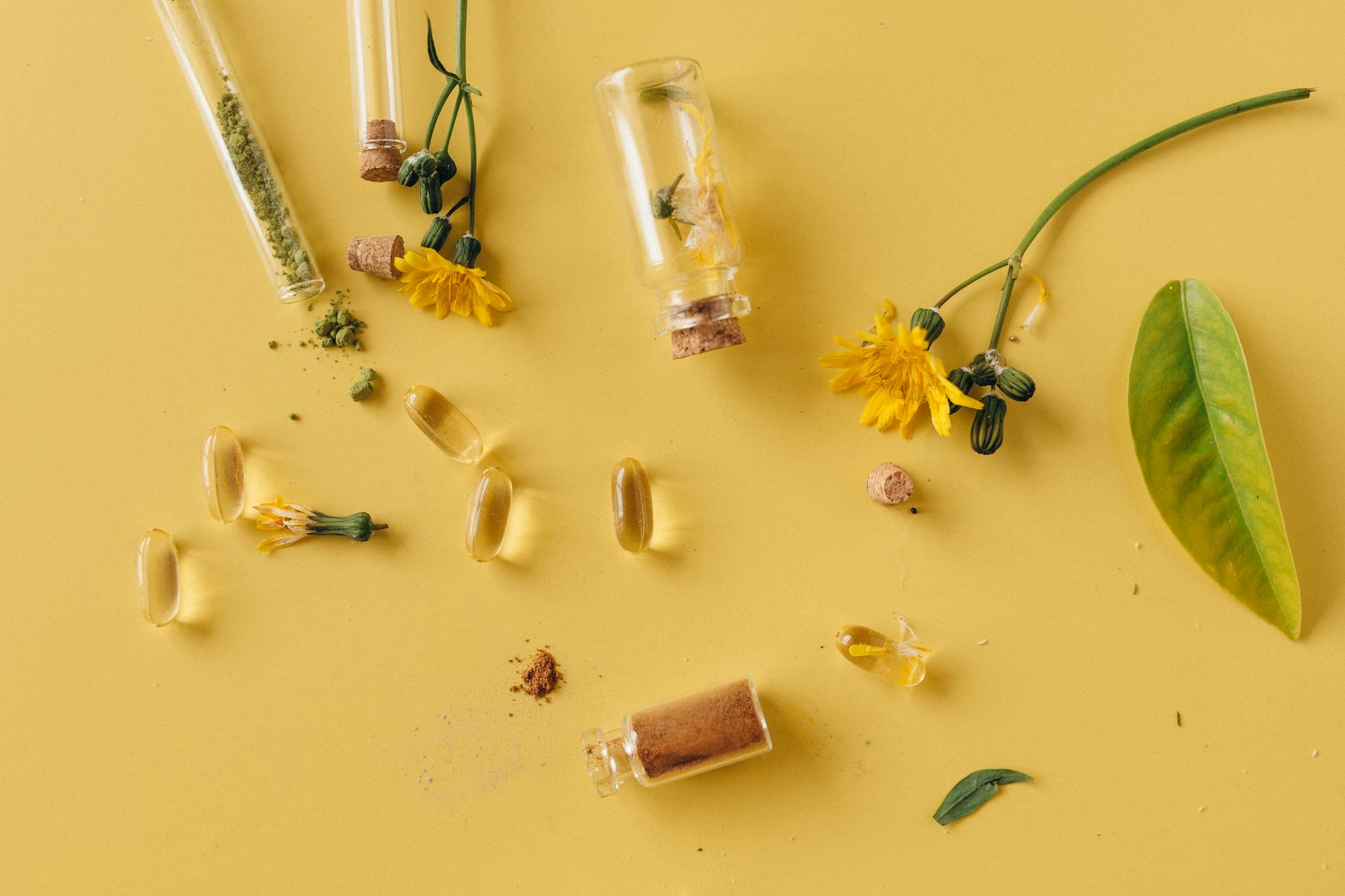 A flat lay of glass bottles, capsules, and flowers on a vibrant yellow surface, representing natural remedies.