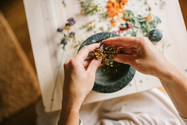 Close-up of hands mixing dried herbs with a mortar and pestle for herbal medicine preparation.